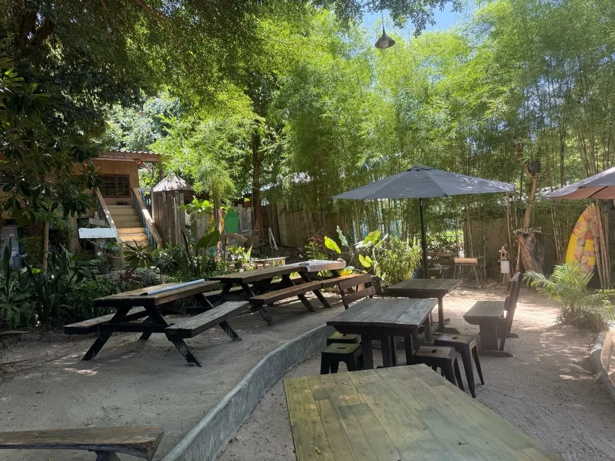 Mesas de madera bajo los árboles en el Samed Coco Bar